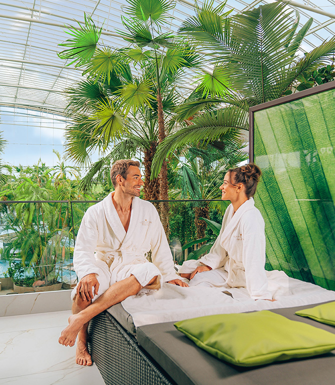 A couple in their private lounge, surrounded by exotic palm trees and water.