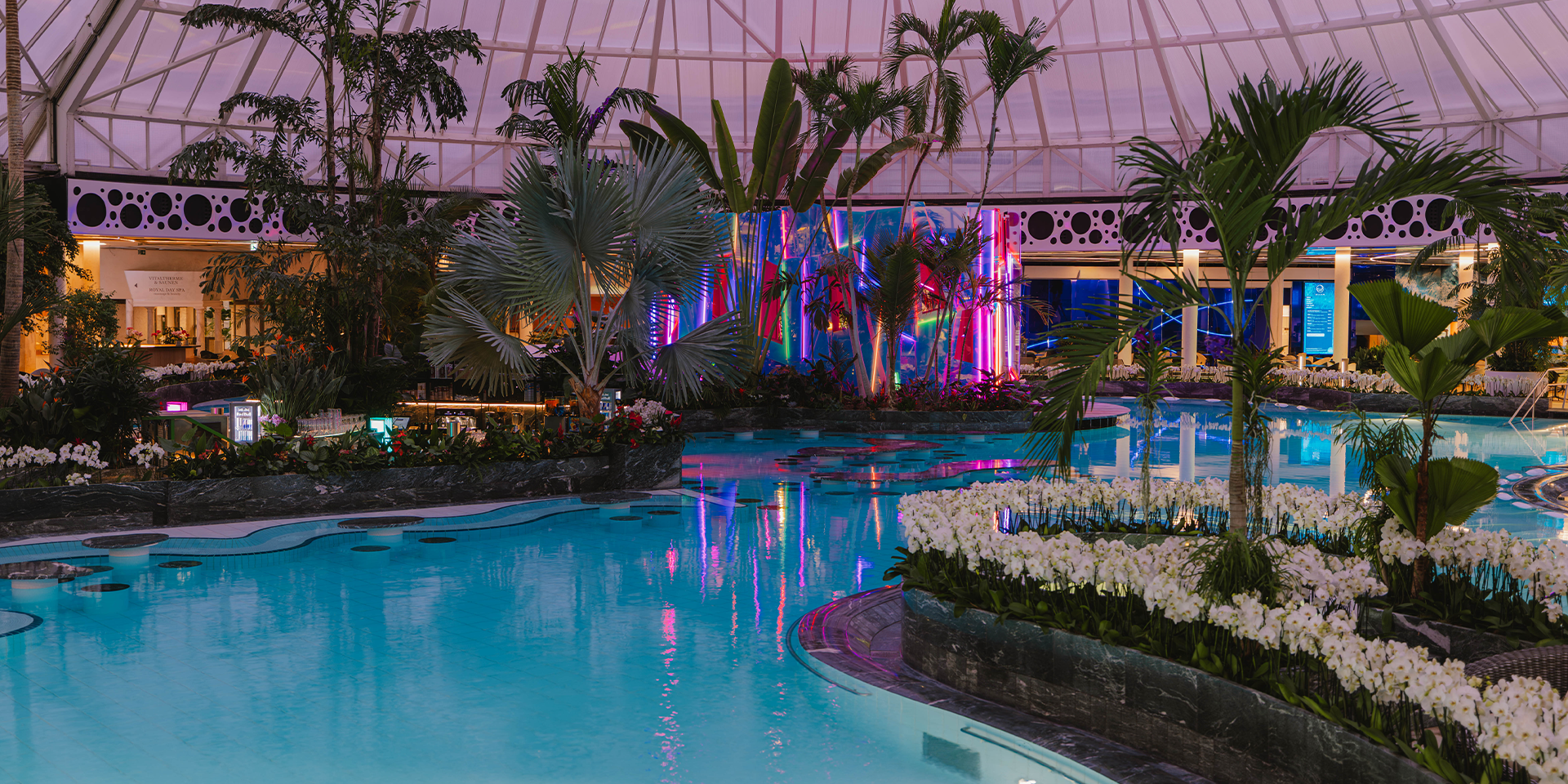 Abendstimmung am großen Thermenbecken, im Hintergrund leuchtet die Re-flexion Sauna in bunten Farben.