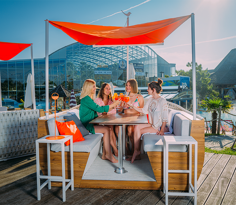 Vier Personen sitzen in einer bootförmigen Lounge mit einem Aperol Spritz in der Hand. 