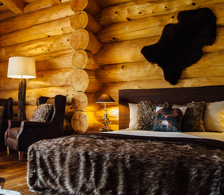 A large bed with brown fur blankets in a wooden chalet with a bearskin on the wall