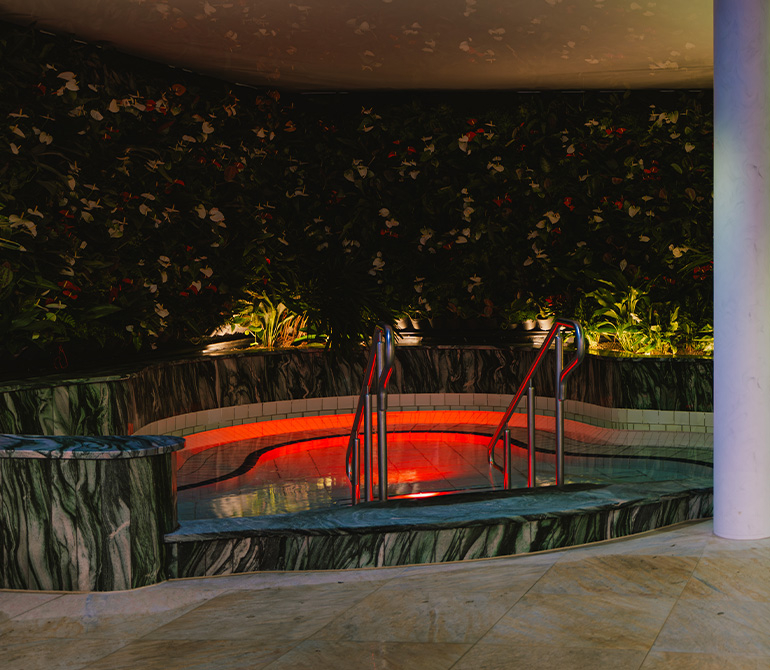 Round pool with red lighting, surrounded by green plant walls.
