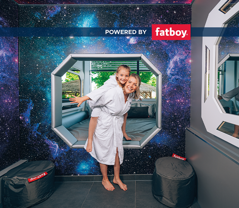 Frau mit Kind stehen vor einer Liegefläche in einem Raum mit Weltraumdesign.