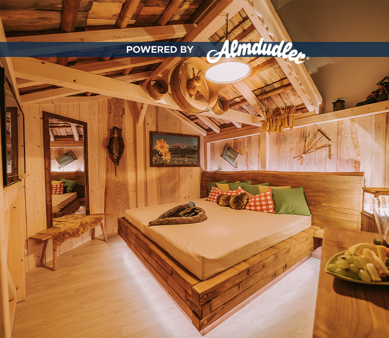 Ein großes Bett mit vielen Kissen und Decke in einem gemütlich beleuchteten Raum im Holz-Hüttenstil.