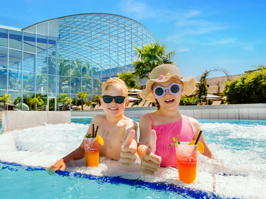 Two kids wearing sunglasses are sitting in the pool with a drink. 