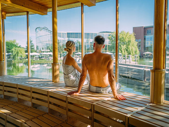 Ein Pärchen sitzt in einer Sauna mit großer Glasfront und genießt den Ausblick.