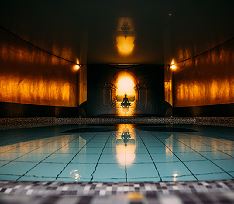 A person sits meditating in front of an illuminated meditation pool at the Erding Thermal Baths, their reflection visible in the water