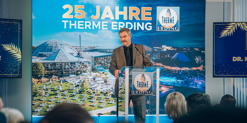 Mann spricht bei Pressekonferenz zum 25-jährigen Jubiläum der Therme Erding vor großem Hintergrund mit Schriftzug '25 Jahre Therme Erding'