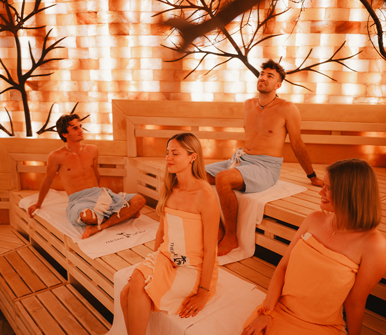 Four guests are sitting in a sauna with orange salt stones on the walls.