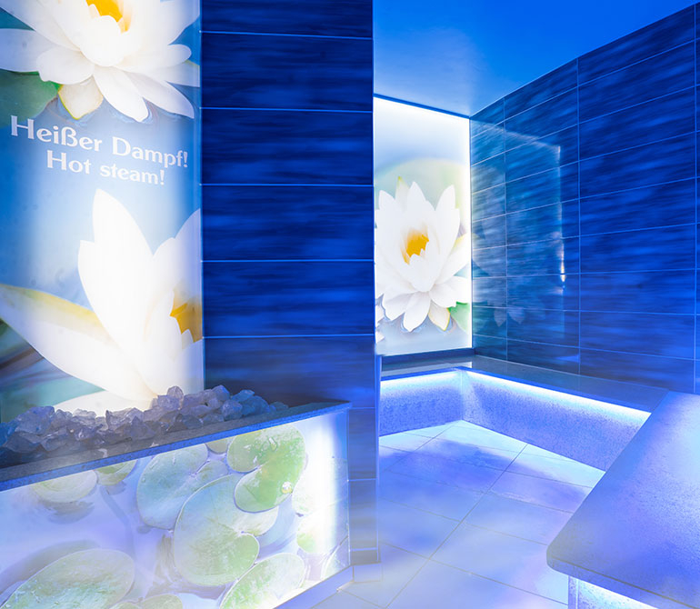 Steam room with blue tiles and illuminated white water lily motifs.