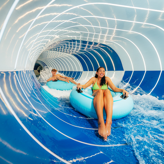 Zwei Gäste rutschen auf einem Wasserreifen in einer Röhrenrutsche.