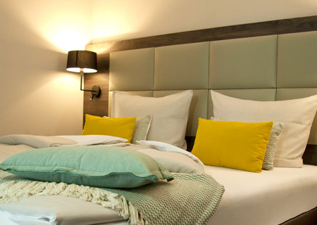 Großes Queensize Bett mit gelben Kissen und grüner Decke.