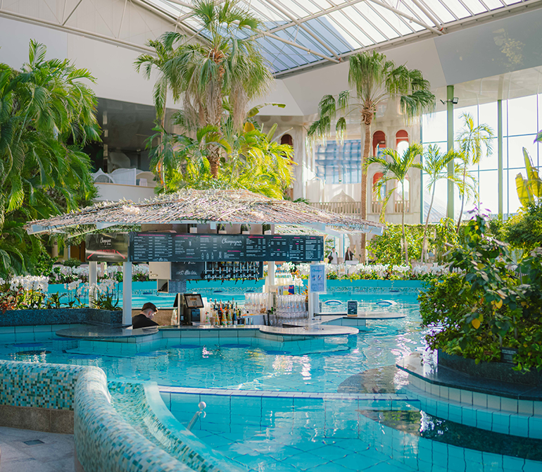 Poolbar mit grünem Blätterdach in der VitalTherme der Therme Erding, umgeben von Wasser und Palmen