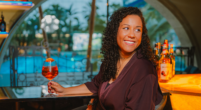 Frau sitzt an Bar mit Cocktail und lächelt