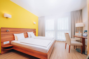 Hotelzimmer Bellezza mit Doppelbett, Stockbetten, Fernseher und Tisch, umgeben von gelben Wänden