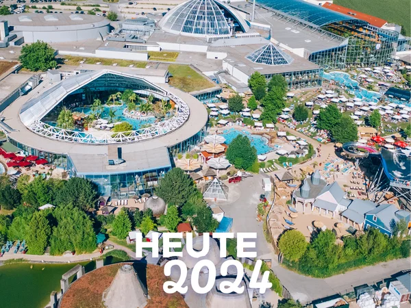 Luftaufnahme der Therme Erding mit Rutschen und Pools, parkähnlich gestaltet. Text: "HEUTE 2024". Früher vs. heute.